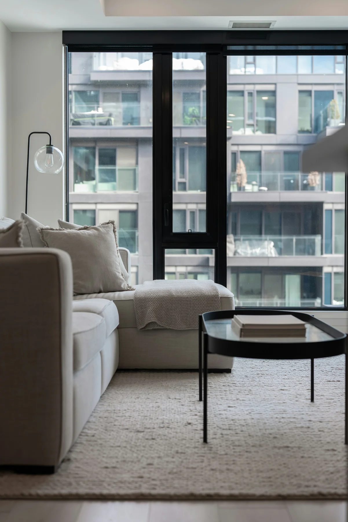 Apartment seating with a pale sofa, round coffee table, broad rug and large windows