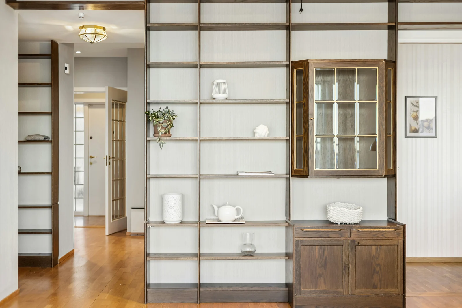 Pale interior walls and shelving beside a warm wood floor and darker wood cabinet